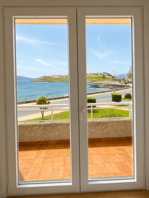 Puertas de cristal con vistas al mar de la costa de Baiona, playa y montañas desde el balcón del apartamento As Estelas