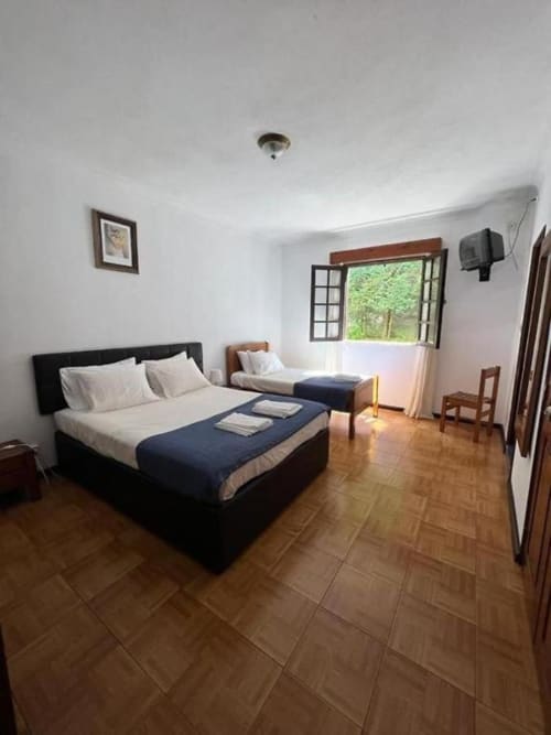 Quarto Triplo Padrão espaçoso na Serrana Gerês Inn com cama de casal, cama individual, piso em azulejo e janela com vista para o jardim