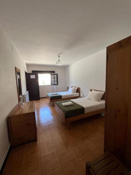 Quarto familiar da Pousada Serrana Gerês com duas camas, móveis em madeira, piso azuleijado e vista para as montanhas pela janela