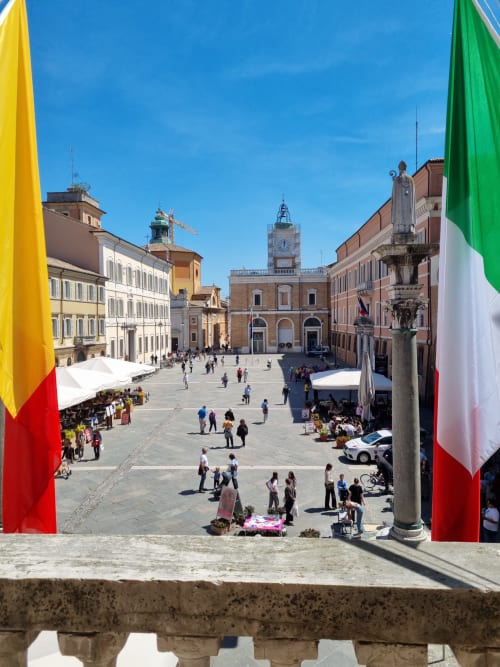 Piazza San Francesco in Ravenna, Italy with historic buildings, clock tower, and Italian flags framing the scenic square