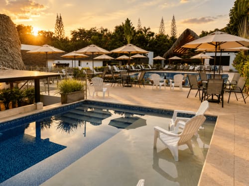 Piscina del resort La Masia Hotel Boutique al atardecer en Anapoima con tumbonas blancas y zonas de descanso con sombrilla