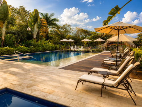 Área de piscina del Hotel Boutique La Masia en Anapoima con tumbonas, sombrillas y jardines tropicales bajo cielo azul