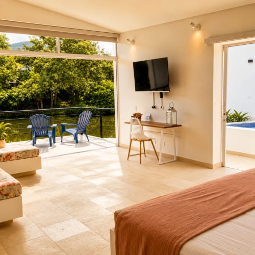 Suite Deluxe espaciosa en La Masia Hotel con terraza vista al lago, sillas Adirondack azules, TV pantalla plana, escritorio y baño privado