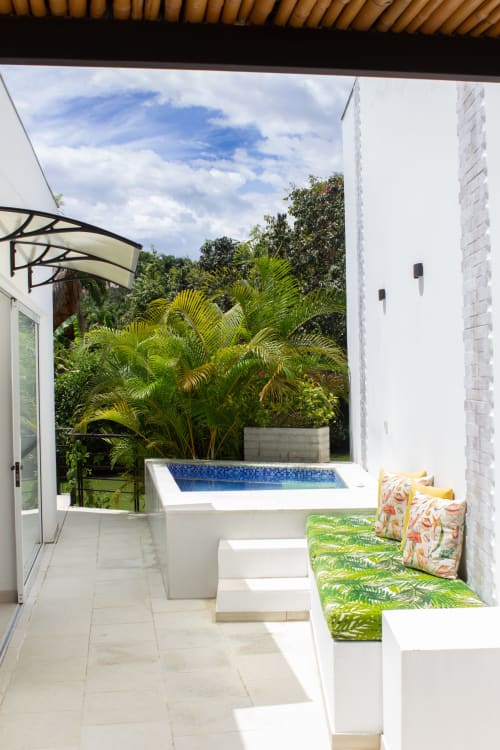 Terraza moderna con jacuzzi privado, asientos verdes acolchados, vistas al jardín de palmeras y fuente de agua azul en La Masia Hotel