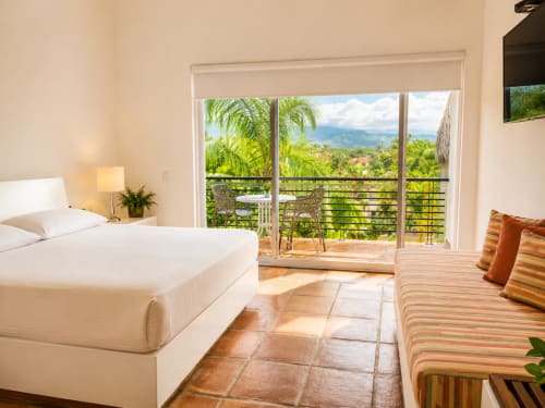 Luminosa habitación Superior en La Masia Hotel Boutique de Anapoima con cama king, sofá a rayas y balcón con vista al jardín