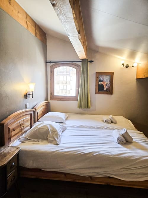 Chambre confortable du refuge Les Étoiles de La Plagne avec lit en bois, poutres apparentes inclinées et fenêtre cintrée