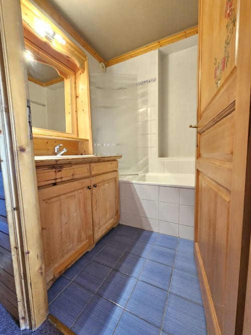 Salle de bains avec meuble vasque en bois, miroir et douche-baignoire carrelée blanche aux Étoiles de la Plagne