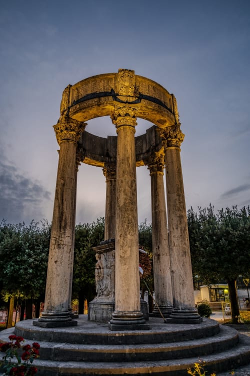 Antica rotonda in pietra con colonne corinzie e capitelli decorativi, illuminata al tramonto in Italia