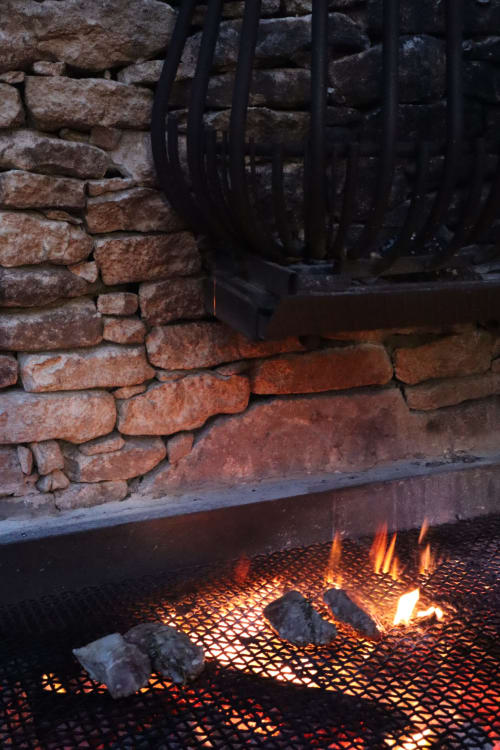 Foyer accueillant à la Cara Lenna B&B de Bonifacio avec flammes scintillantes, mur en pierre et zone de repos avec grille métallique.