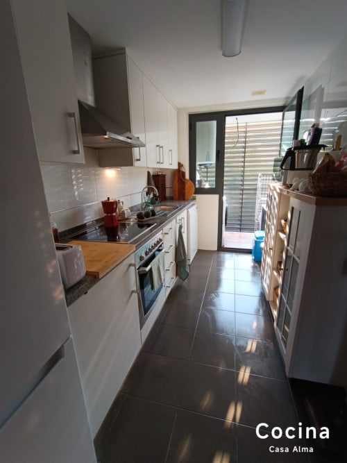 Cuisine blanche moderne avec sol en carrelage sombre, électroménagers en acier inoxydable et portes vitrées donnant sur le balcon de Casa Alma