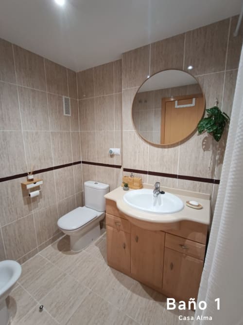 Salle de bain moderne à Casa Alma à Sant Jordi avec meuble-lavabo en bois, miroir rond, lavabo blanc et carrelage beige