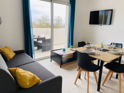 Elegante appartamento a Résidence Marina di Bravone con tavolo da pranzo, divano grigio, cuscini gialli e balcone con vista mare