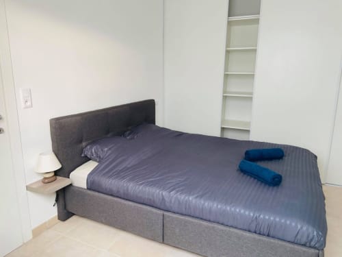 Accogliente camera da letto presso Résidence Marina di Bravone con letto grigio, lampada da comodino, scaffalature bianche e asciugamani blu