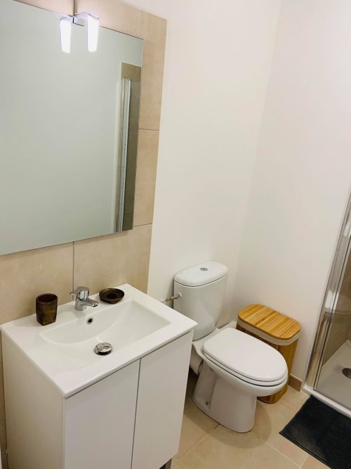 Bagno moderno della Résidence Marina di Bravone con lavabo bianco, wc con sedile in legno e specchio incorniciato