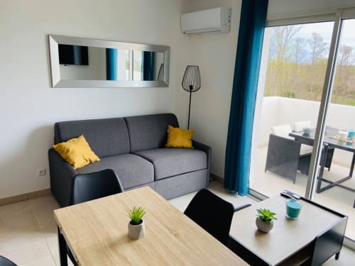 Accogliente appartamento moderno a Résidence Marina di Bravone con divano grigio, tavolo da pranzo e balcone con vista sulla natura
