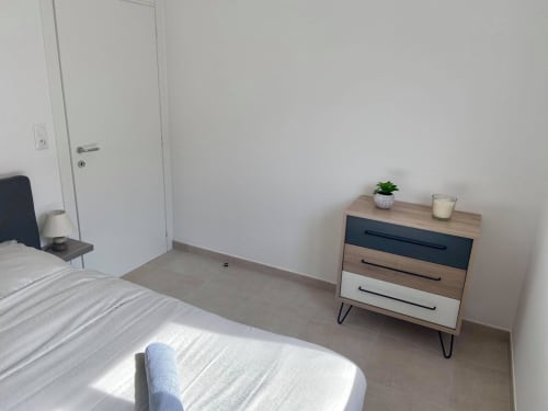 Chambre moderne à la Résidence Marina di Bravone avec lit, commode en bois, plante en pot et murs blancs