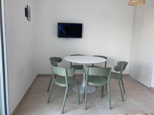 Modern meeting room at Résidence Marina di Bravone with round white table, green chairs, wall-mounted TV, and wicker pendant