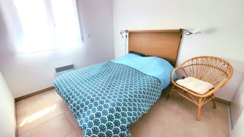 Cozy bedroom in Marina di Bravone apartment, Linguizzetta, with wooden bed, blue patterned bedding, and wicker chair