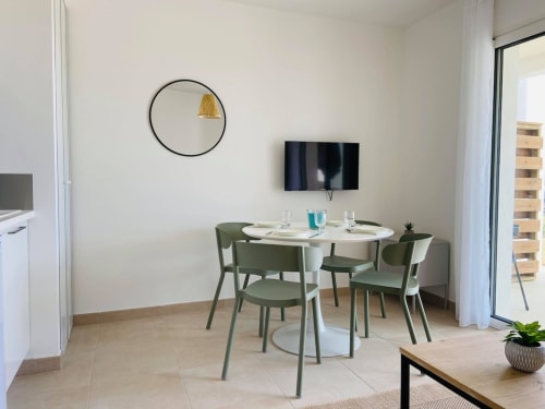 Modern dining area in Marina di Bravone apartment with round table, green chairs, wall-mounted TV, and coastal view access