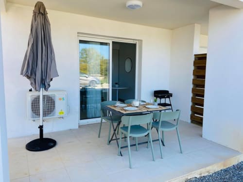 Modern patio at Résidence Marina di Bravone with dining table, turquoise chairs, AC unit, umbrella, and sea view doors.