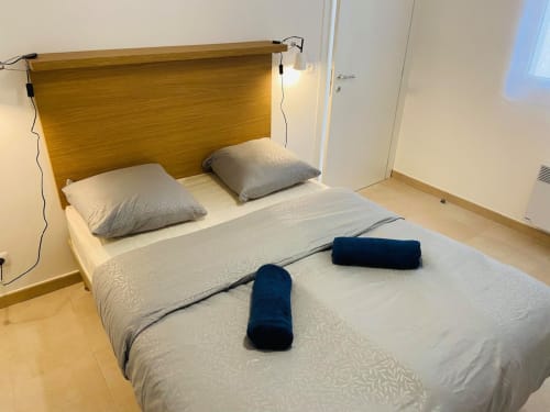 Modern bedroom at Résidence Marina di Bravone with wooden headboard, grey pillows, and rolled towels on bed
