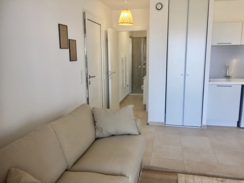 Studio moderne à la Résidence Marina di Bravone avec canapé beige, kitchenette et couloir vers la salle de bain