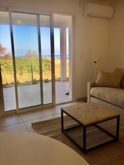 Studio moderne à Marina di Bravone avec vue mer, mobilier beige, table en bois et accès direct à la plage par portes vitrées