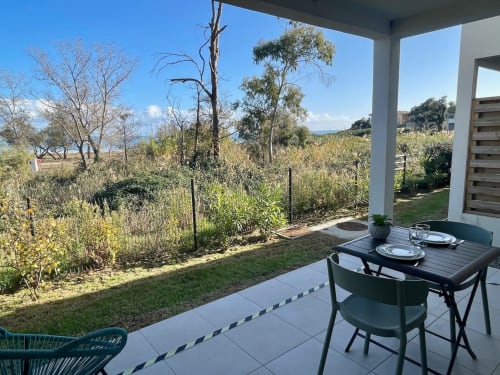 Patio moderne à la Résidence Marina di Bravone avec table de salle à manger dominant les jardins et vue mer près de Linguizzetta