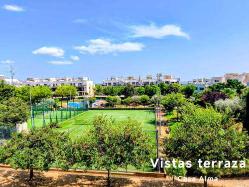 Vue de la terrasse de Casa Alma à Sant Jordi avec terrain de sports, piscine et communauté résidentielle dans un cadre verdoyant