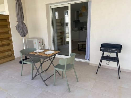 Patio du studio à la Résidence Marina di Bravone avec table à manger, chaises, barbecue, et vue sur la cuisine et les portes.