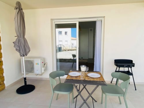 Patio du studio à la Résidence Marina di Bravone avec table de repas, chaises vertes, barbecue et portes donnant sur la plage à Linguizzetta