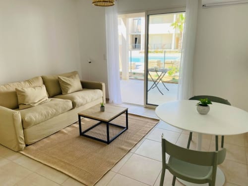 Studio moderne à Marina di Bravone avec canapé beige, table de salle à manger et balcon vue piscine surplombant la plage