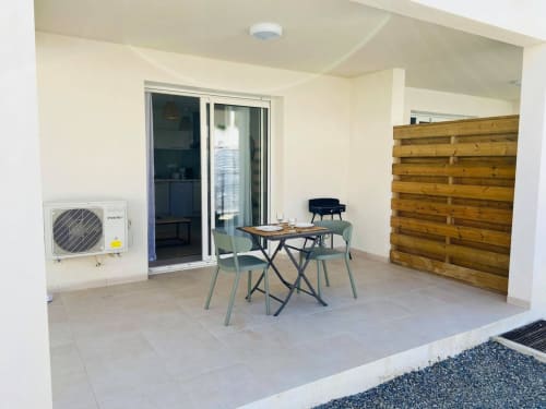 Modern studio apartment patio at Résidence Marina di Bravone with dining table, chairs, AC unit, and wooden privacy screen