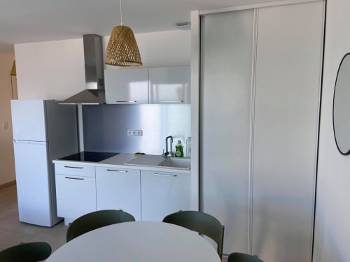 Modern kitchen in Marina di Bravone apartment with white cabinets, stainless steel appliances, woven pendant light, and