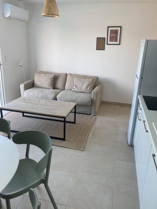 Modern living room at Résidence Marina di Bravone with beige sofa, wooden table, and kitchen area