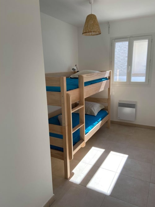 Chambre lumineuse avec lits superposés en bois, matelas bleus et luminaire suspendu tissé à la Résidence Marina di Bravone à Linguizzetta