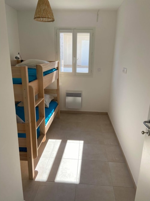 Chambre lumineuse en bord de mer à la Résidence Marina di Bravone avec lits superposés en bois, linge bleu, portes vitrées et carrelage