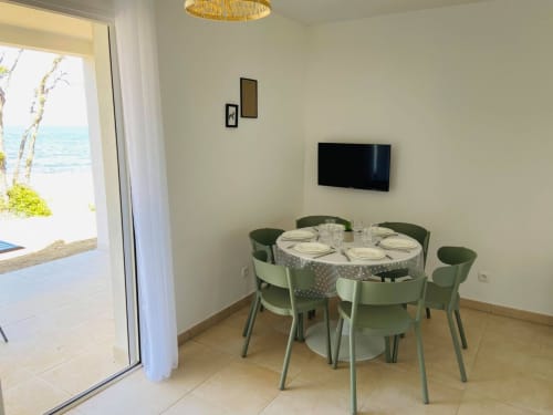 Salle à manger de l'appartement en front de mer à Marina di Bravone avec table ronde, chaises vertes et vue sur la mer depuis la porte-fenêtre