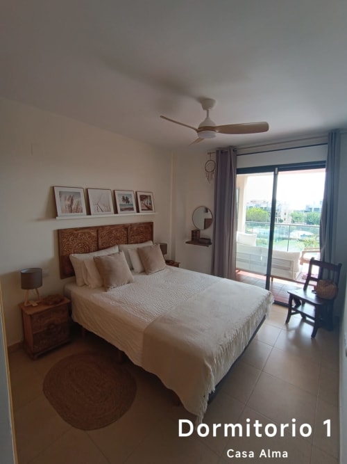 Chambre lumineuse avec lit double, tête de lit en bois, ventilateur de plafond et balcon avec vue sur la piscine à Casa Alma, Sant Jordi