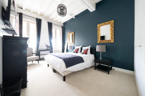 Chambre luxueuse au Pavillon Des Millesimes à Lussac avec murs bleu-vert, miroirs dorés, literie blanche et vue sur la ville