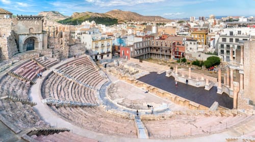 Ruinas de anfiteatro romano en Cartagena, España con paisaje urbano histórico y montañas al fondo