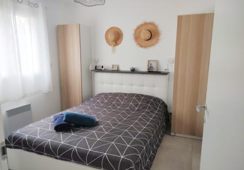 Camera moderna presso Résidence Marina di Bravone con biancheria geometrica, dettagli in legno e cappelli di paglia come decorazione murale