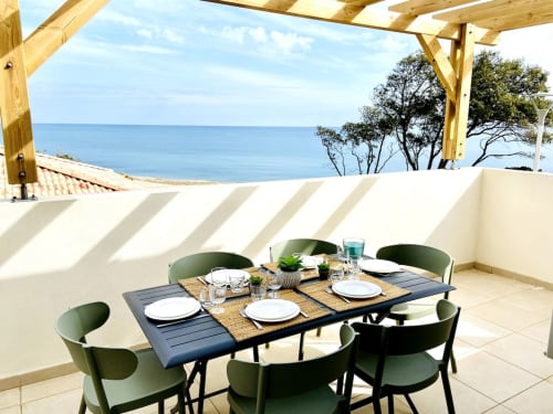 Seaside terrace dining at Résidence Marina di Bravone with ocean view, wooden pergola, and table set for six