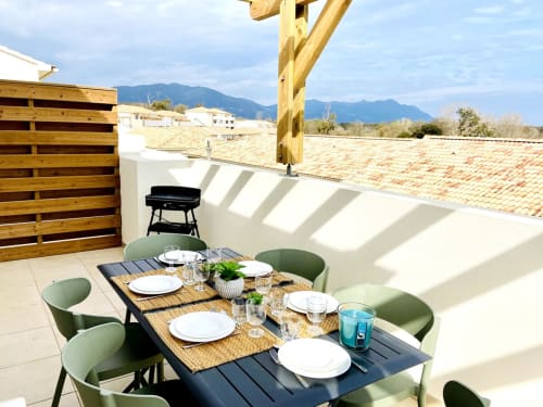 Rooftop dining terrace at Résidence Marina di Bravone with table setting, mountain views, wooden pergola, and grill in