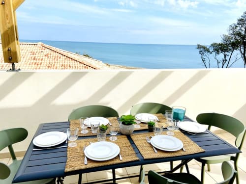 Seaside dining setup at Résidence Marina di Bravone with ocean view, place settings, and green chairs