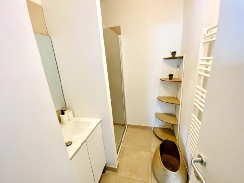 Modern bathroom at Résidence Marina di Bravone with sink, shower, wooden shelves, and heated towel rack