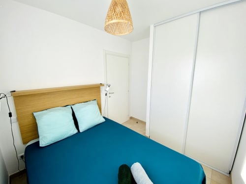 Modern bedroom at Résidence Marina di Bravone, Linguizzetta, with wooden bed frame, turquoise bedding, and woven pendant