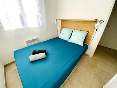 Bright bedroom at Résidence Marina di Bravone with blue bedding, wooden headboard, light pillows, and tiled floor near