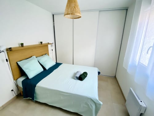 Chambre moderne à la Résidence Marina di Bravone avec lit en bois, coussins bleu clair, plaid bleu marine, luminaire suspendu tissé, et