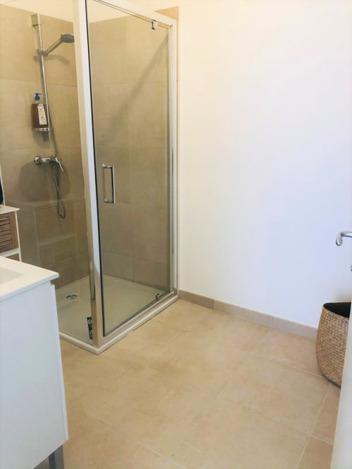 Salle de bains moderne avec douche italienne en verre, carrelage beige, vasque blanche et panier tressé à la Résidence Marina di